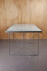 Retro IKEA dining table with metal frame and smoked glass top against a cedar wood backdrop and a concrete floor.
