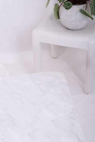 Detailed shot from above showing the corner of the marble coffee table. Next to the table is a white kartell plastic chair with a plant on the seat.