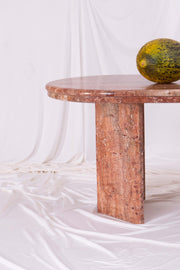 Detail shot of organge marble coffee table leg against white drapes. A melon sits on the tabletop. 
