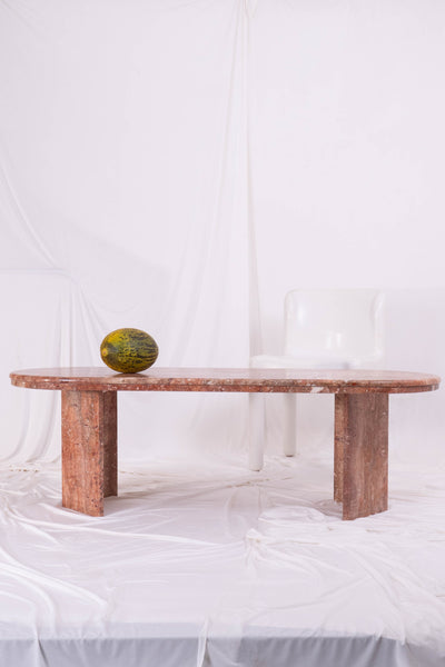 Rust coloured marble coffee table with melon on top. Set against white drapes.