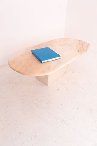 Oval pink marble table with a blue book on a white floor