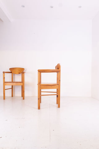 Two vintage pine carver chairs on a white floor and white wall