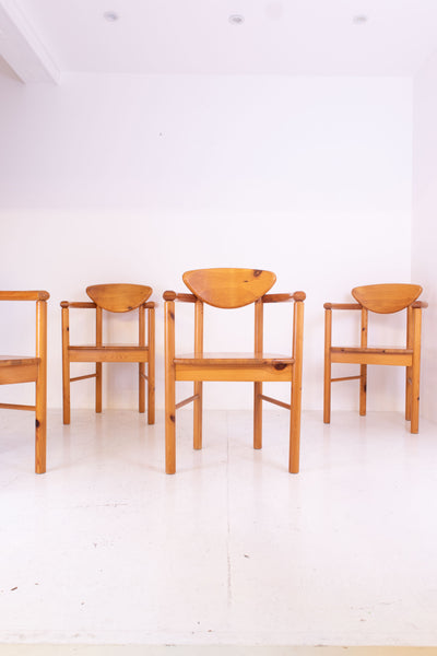 Four vintage pine carver chairs on a white floor with a white wall background.