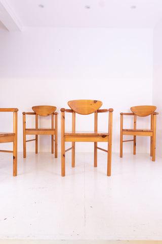 Four vintage pine carver chairs on a white floor with a white wall background.