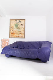 Vintage purple leather sofa in a room with a white wall and a framed picture.