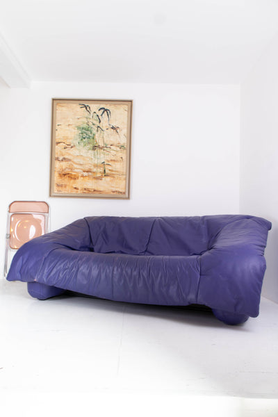 Vintage purple leather sofa in a room with a white wall and a framed picture.