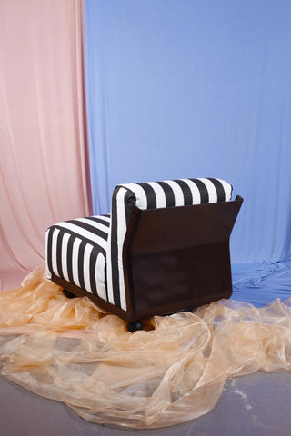 rear of vintage Amanta chair with brown frame and black and white striped upholstery against pink and blue draped backdrop.  