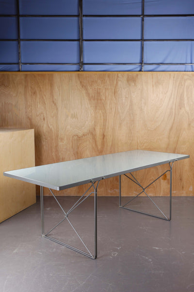 Vintage Moment dining table by Neils Gammelgaard for IKEA against cedar panels, concrete floor and a blue drape. 