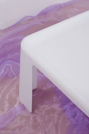 Close up of tapered leg design of this white Amanta coffee table. It is shot against a purple chiffon floor covering. 