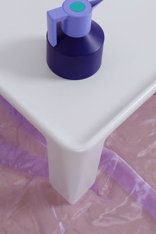 Overhead view of white retro Italian coffee table against a purple chiffon floor covering. A two-tone, purple coffee pot sits on top of the Amanta table. 