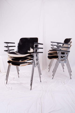 Six metal stacking chairs by Piretti for Castelli stacked in two piles. Set against a white backdrop.