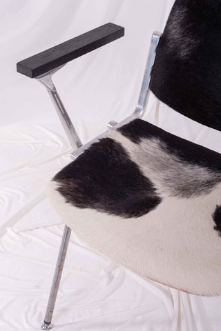 Detail picture of cowhide seat on a vintage metal stacking chair. Set against a white backdrop. 