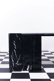 Detailed shot of leg of black marble coffee table with white veining against a white backdrop and a chequered floor.