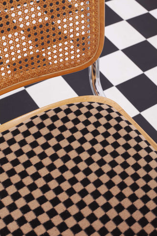 Detailed image of vintage Cesca cantilevered chair with cane seat back and upholstered seat against a chessboard backdrop. 