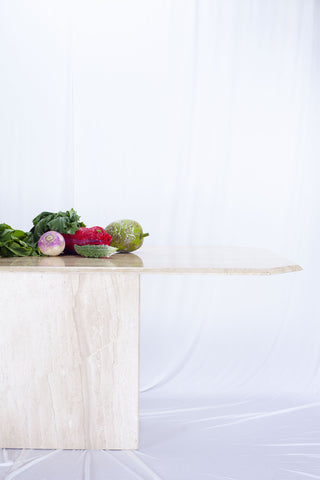 Large stone dining table with vegetables on the surface. White drapes in the background