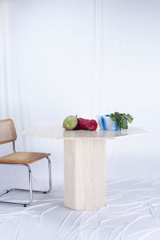 Vintage Italian octagonal travertine small dining table. There are vegetables on top of the table and cesca chair next to the dining table. The background is draped white fabric.