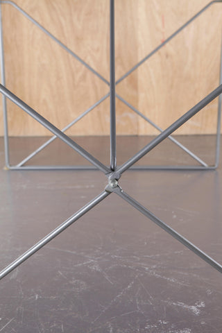 Close up of wire frame of metal Moment dining table by Gammelgaard for IKEA against a cedar and concrete backdrop. 