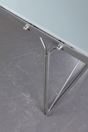 close up of IKEA Moment table with metal frame and smoked glass tabletop against a concrete floor. 