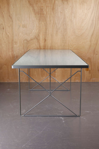 Retro IKEA dining table with metal frame and smoked glass top against a cedar wood backdrop and a concrete floor.