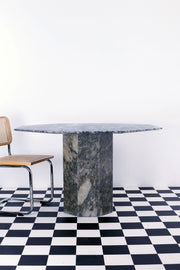 Vintage grey marble dining table with central column against a white backdrop and a black and white floor. A Breuer Cesca chair sits beside the stone dining table. 