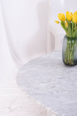 Carrara marble coffee table with daffodils on top. A white plastic chair and white drapes make up the background.