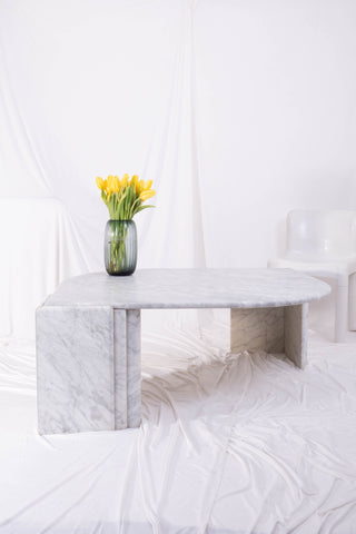 large white marble coffee table with daffodils on top in front of white drapes.