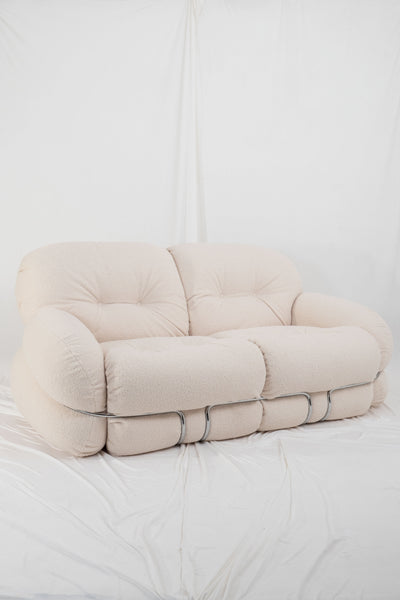 Vintage okay sofa by Piazzesi in cream, bouclé upholstery in front white drapes.