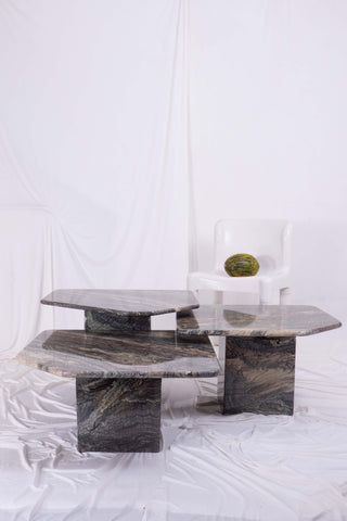 Set of three nesting marble coffee tables with draped white fabric and white plastic kartell chair in the background