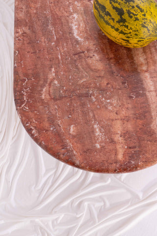 Details shot of the veining of this orange marble coffee table. Set against white drapes.