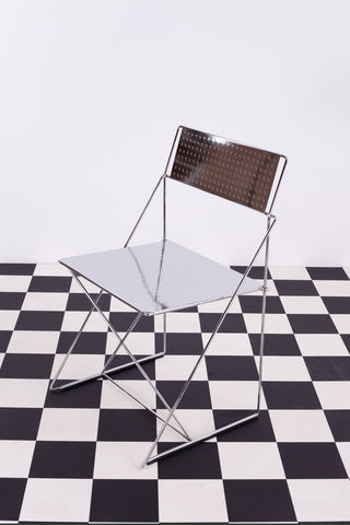 Vintage chrome X-Line chair by Haugesen for Magis against a white wall and a chequered floor.