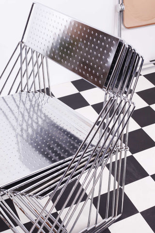 Set of neatly stacked X-Line chairs by Haugesen against a chequered floor and a white background. 